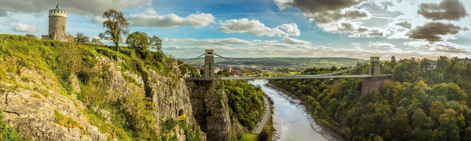 A panorama view looking up the Avon gorge towards Bristol showing the Clifton Observatory, the Clifton Suspension bridge and the Giant's Cave viewpoint on a bright Autumn day