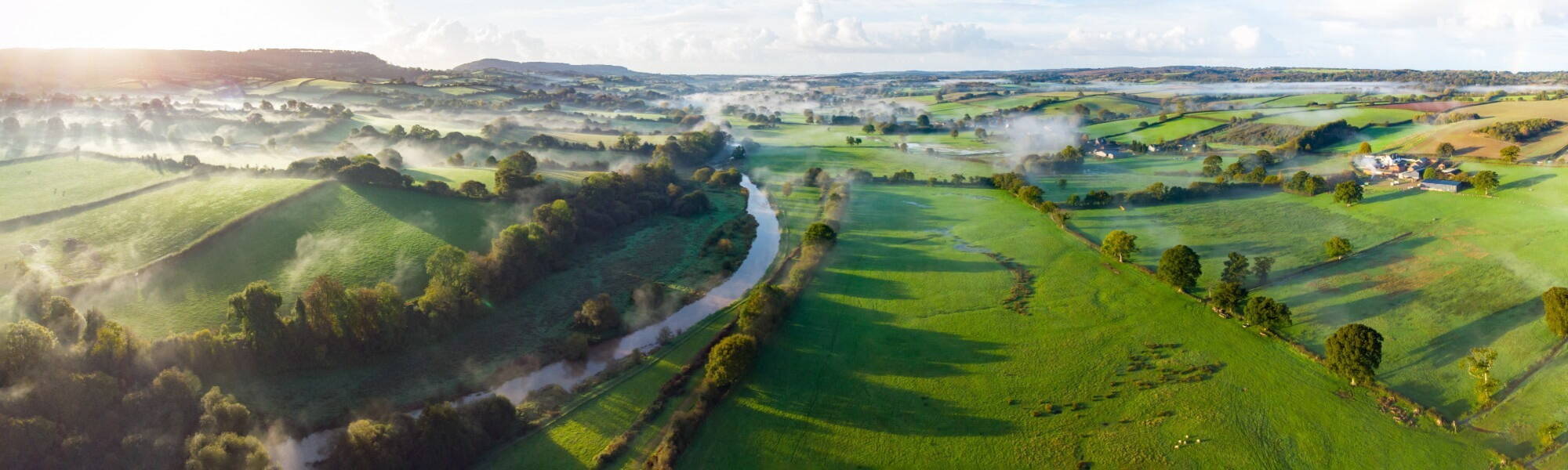 Aerial panorama picture of the river Otter near Honiton and Ottery St Mary. Sunrise and rolling mist cross the lush green fields below. Spectacular landscape