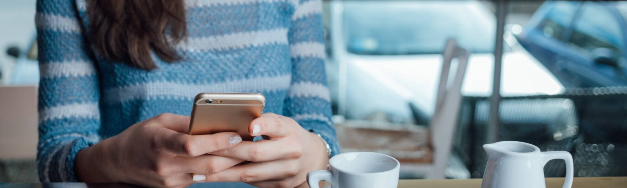 Women wearing blue and white stripey jumper using smartphone whilst sitting down at a table