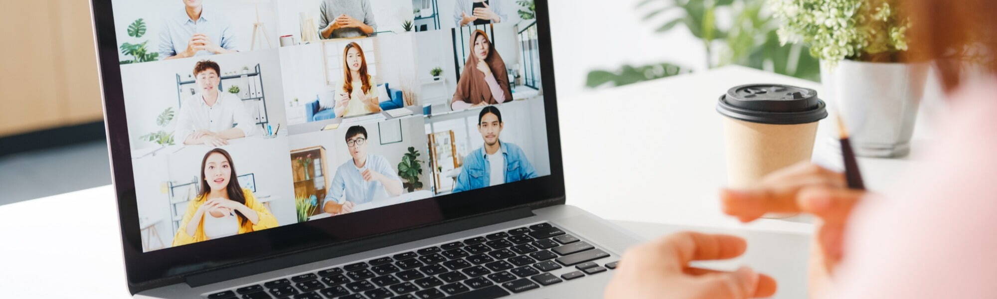 Using a laptop for a relaxed team business meeting with diverse team, connecting over coffee with plant on minimalistic desk