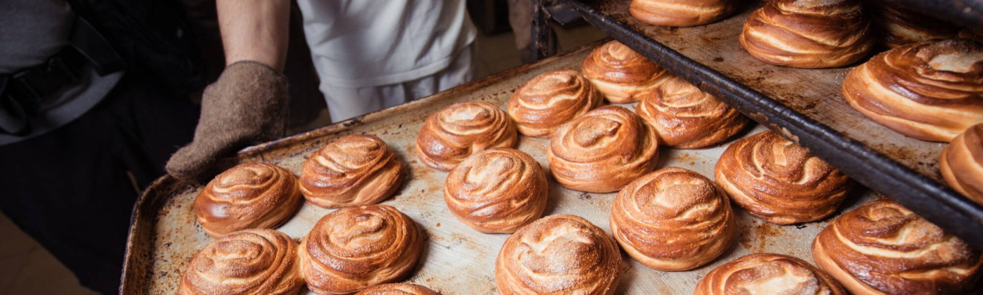 Baker's hands in mittens hold baking sheet with sweet buns