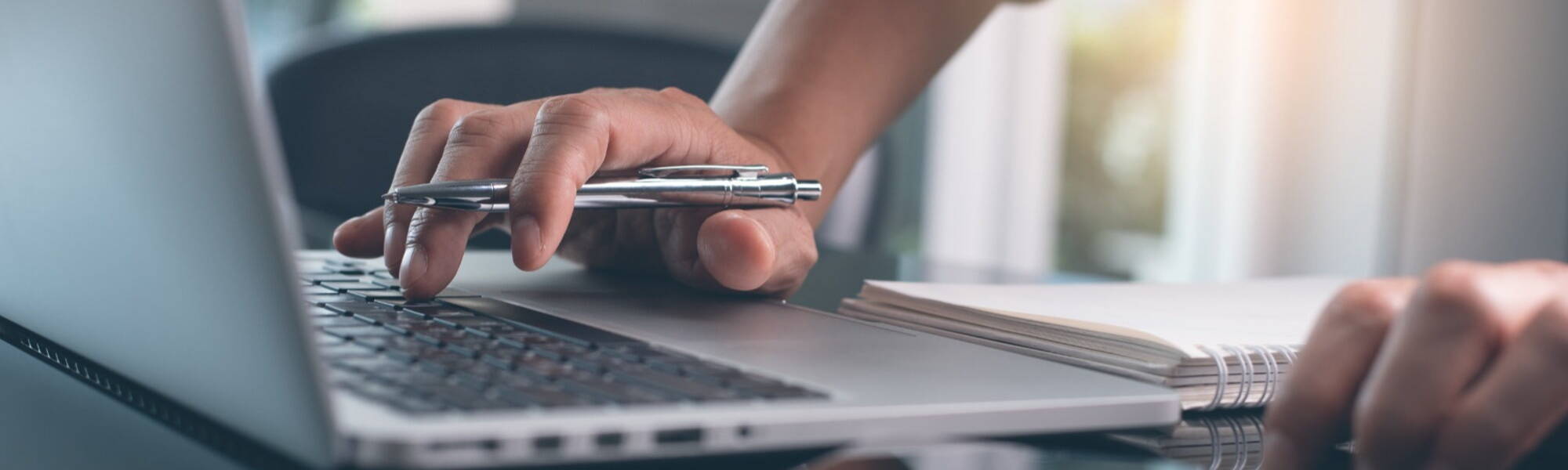 hand typing on laptop holding metal biro pen