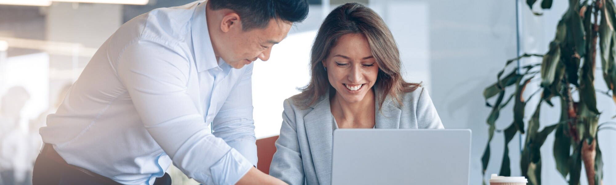 a man and a women in a professional sharing notes over a laptop